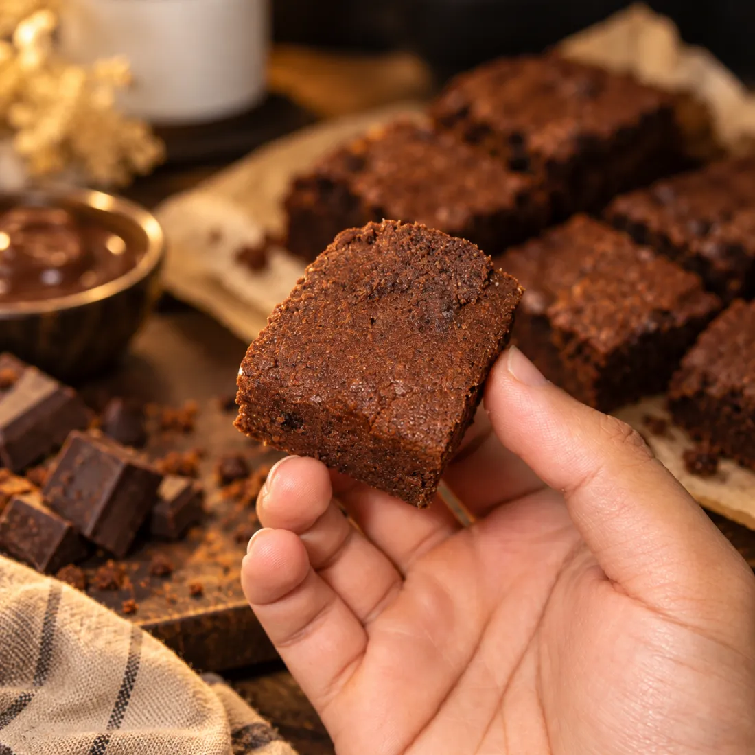 A hand holding a square of fudgy brownie above a tray of cut brownies